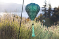"Allsop Stella Balloon Tassel jade solar lantern glowing at night hanging from tree branch over waterfront lawn with city lights reflecting on water"