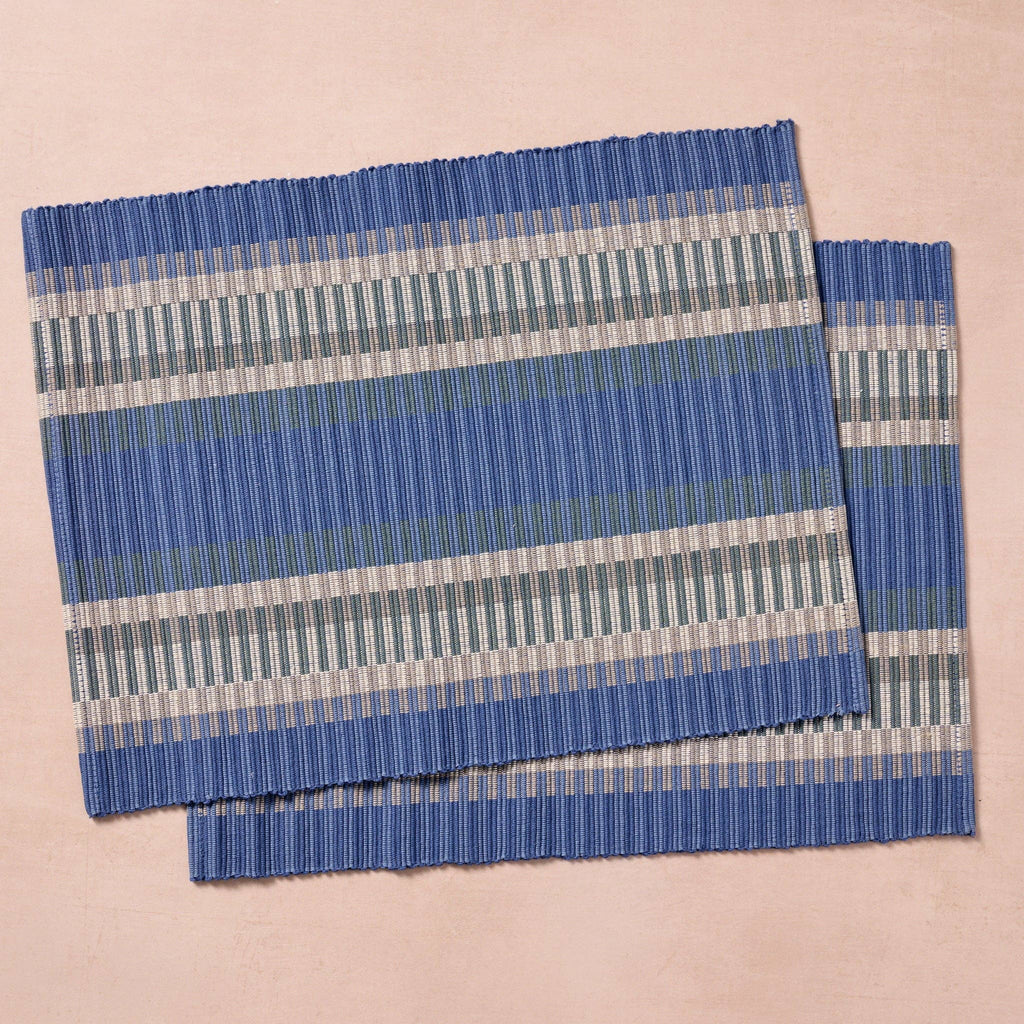 Two placemats laid flat (pink bg): "Set of two blue, gray, and white striped handloomed cotton placemats, handcrafted in Nepal by Ten Thousand Villages artisans