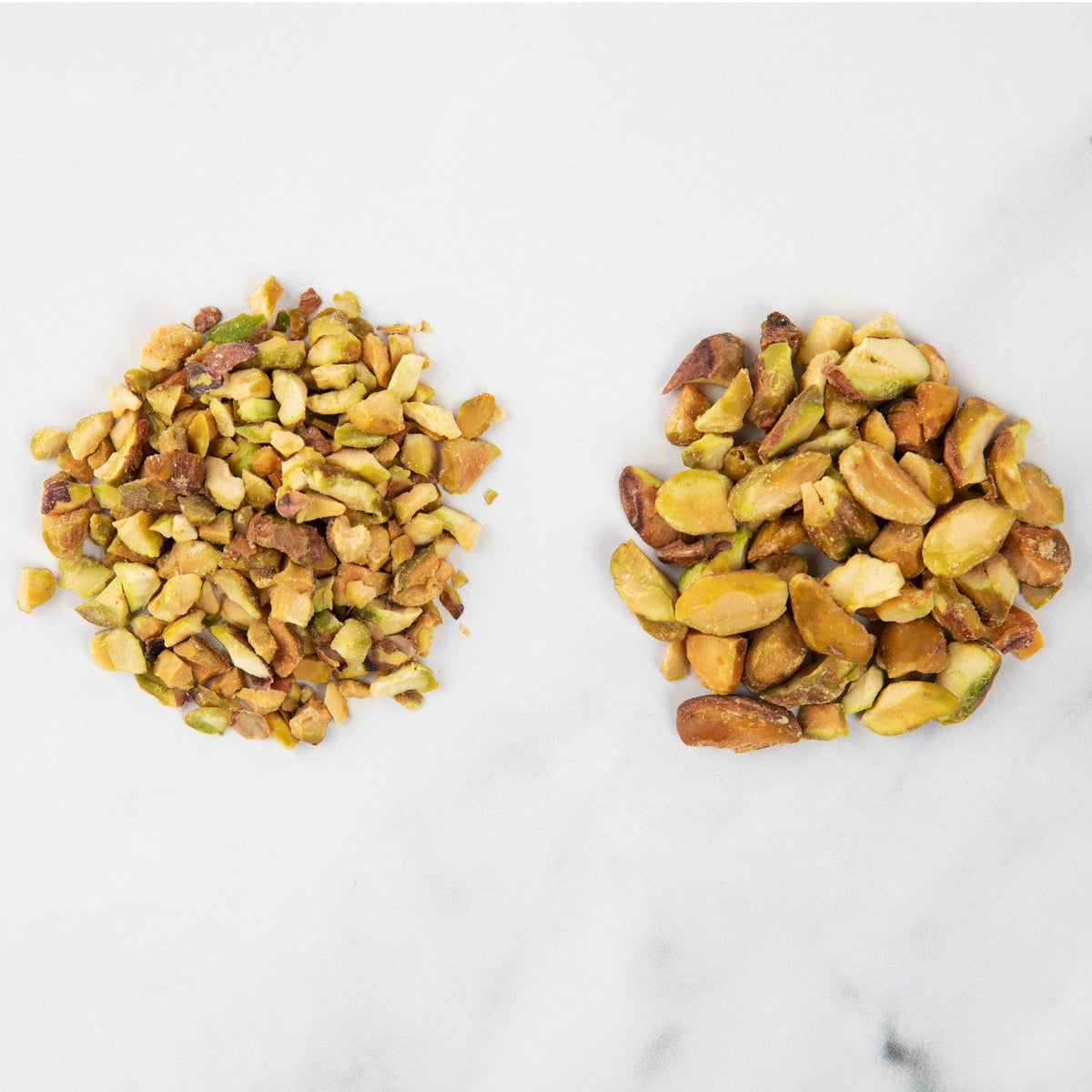 Side-by-side comparison of finely chopped pistachios on the left and coarsely chopped pistachios on the right on a marble surface, showing the two grinding settings of the Progressive nut chopper.