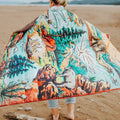Person holding a colorful quilt with nature-themed design on a beach
