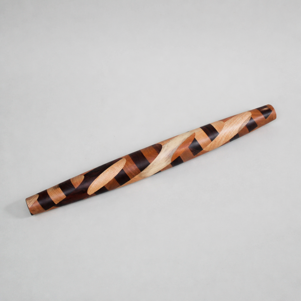  Vendor photo, clean white/grey background, full product shot showing the warm mixed hardwood tones. "Miss Clarissa handmade French rolling pin, mixed hardwood with bold swirling pattern in Black Walnut, Cherry and Maple — The Rileyland Collection, Tennessee"