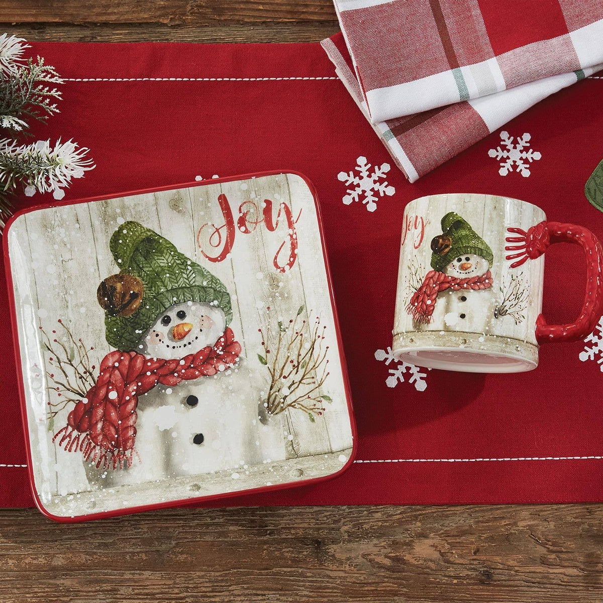 Park Designs Farmhouse Snowman salad plate styled on a red holiday table runner with matching Joy snowman mug, snowflake accents, and plaid napkin"