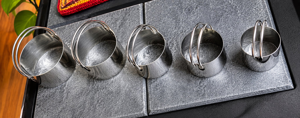 Four stainless steel round biscuit cutters with wire loop handles laid flat on a dark slate surface, showing graduated sizes from small to large — Fox Run