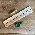 Celtic Farm seeding gift set — engraved hardwood seeding ruler, wooden dibble, and green seed dispenser arranged on a weathered wood surface