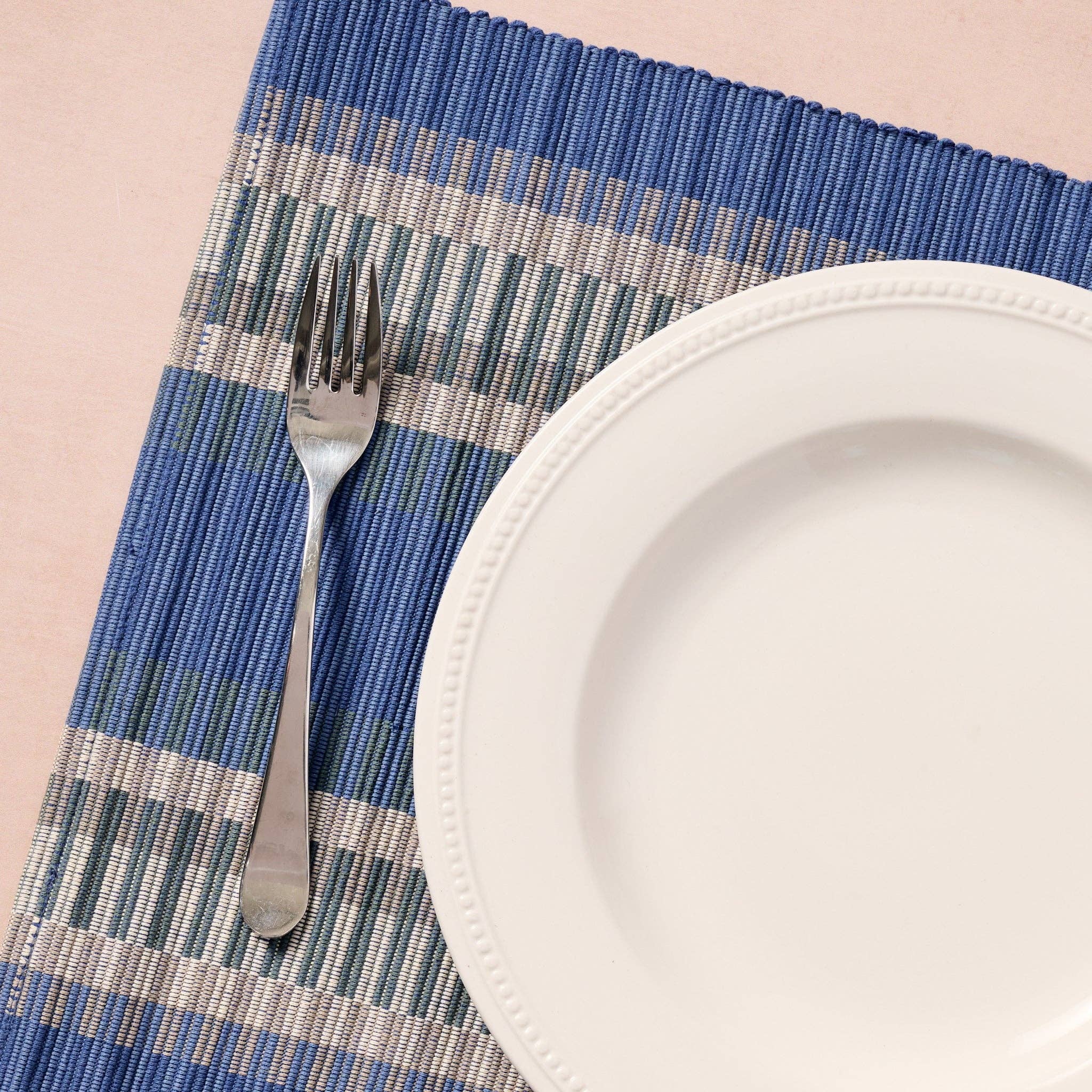 Close-up with fork and white plate: "Close-up of blue striped handloomed cotton placemat styled with a white dinner plate and silver fork"