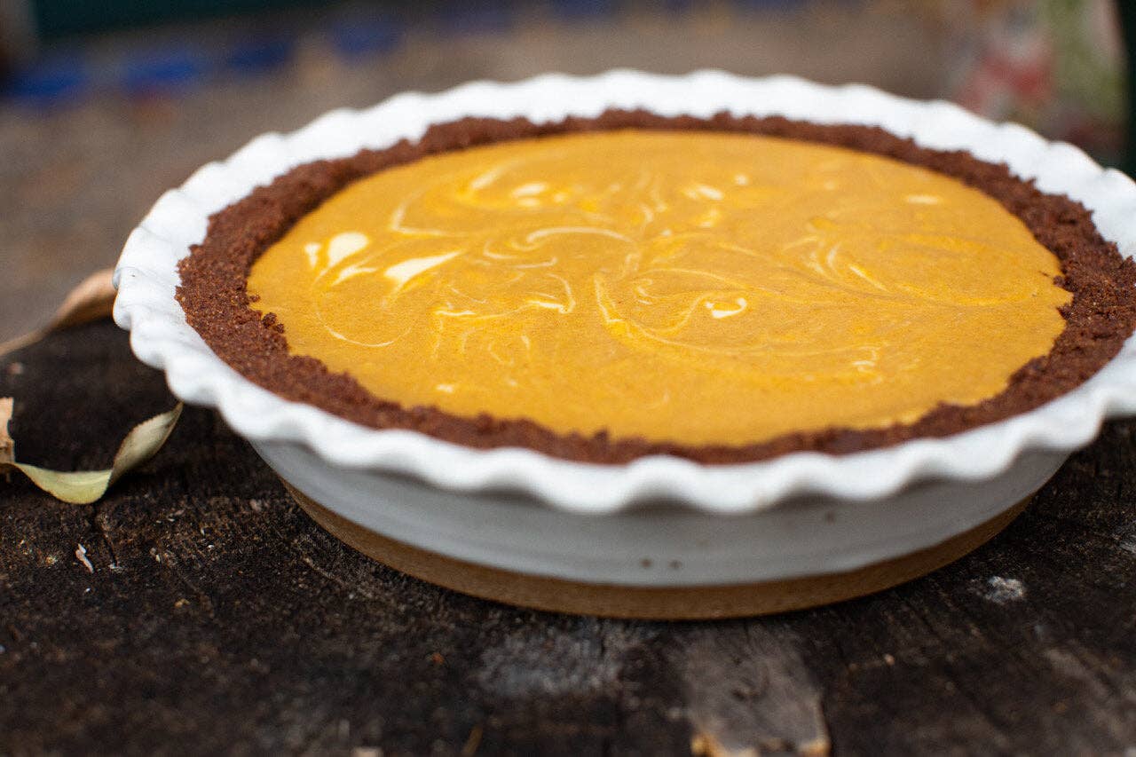 White speckled stoneware pie dish with ruffled edge filled with a golden custard pie in a chocolate cookie crust