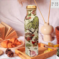 Decorative water bottle with floral and bird pattern on a table with croissants and a vase.
