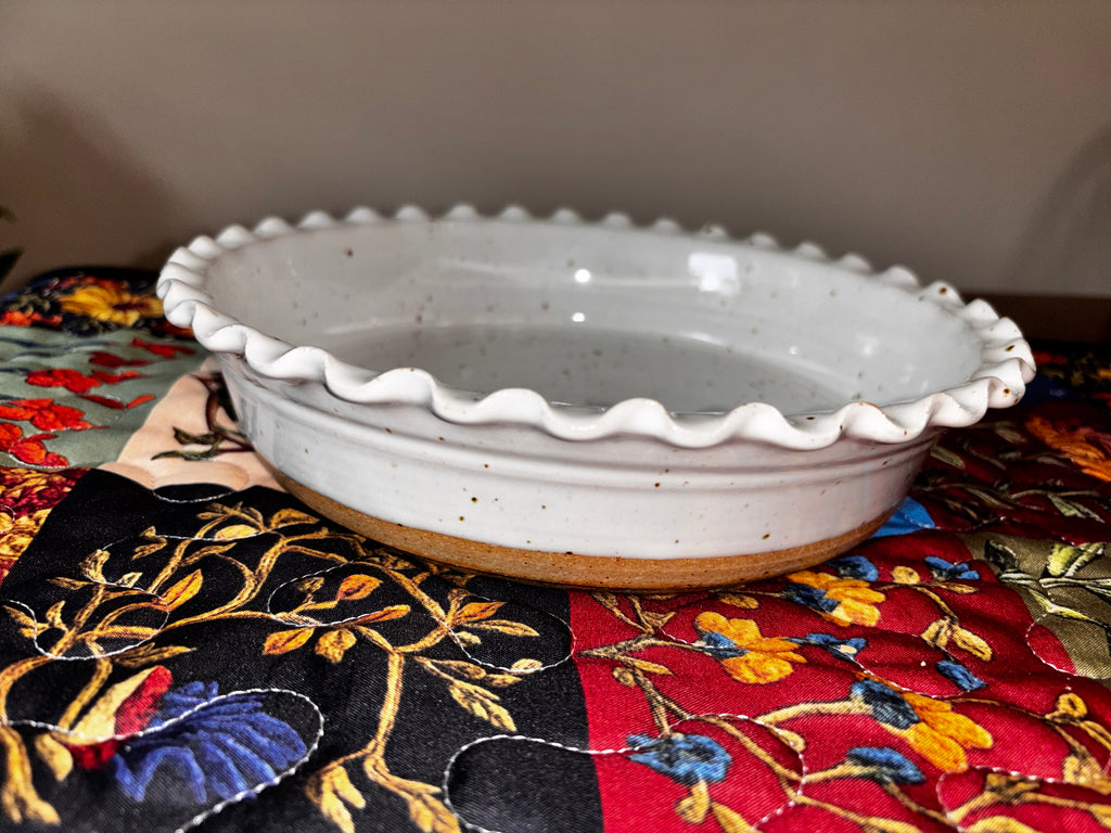  6" straight on) Front view of a 6-inch hand-thrown white speckled stoneware deep dish pie plate with ruffled scalloped edge and unglazed natural clay base
