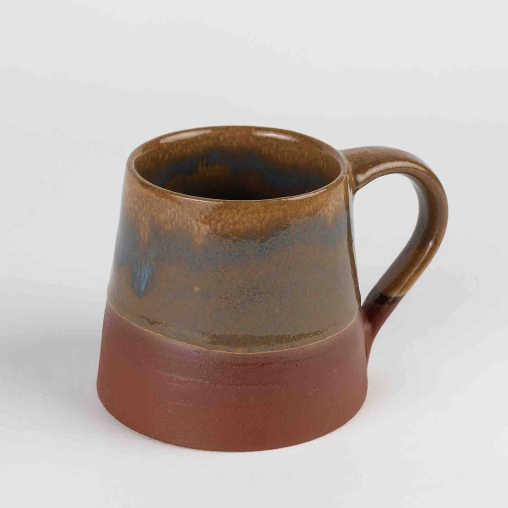 Slightly different angle, handle right (gray bg): "Side view of hand thrown terracotta and brown glazed ceramic mug with blue accent, 12 oz, handcrafted in the Kathmandu Valley"