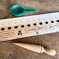 Celtic Farm seeding gift set with engraved hardwood seeding ruler showing plant spacing guides, wooden dibble, and green seed dispenser on a wood surface