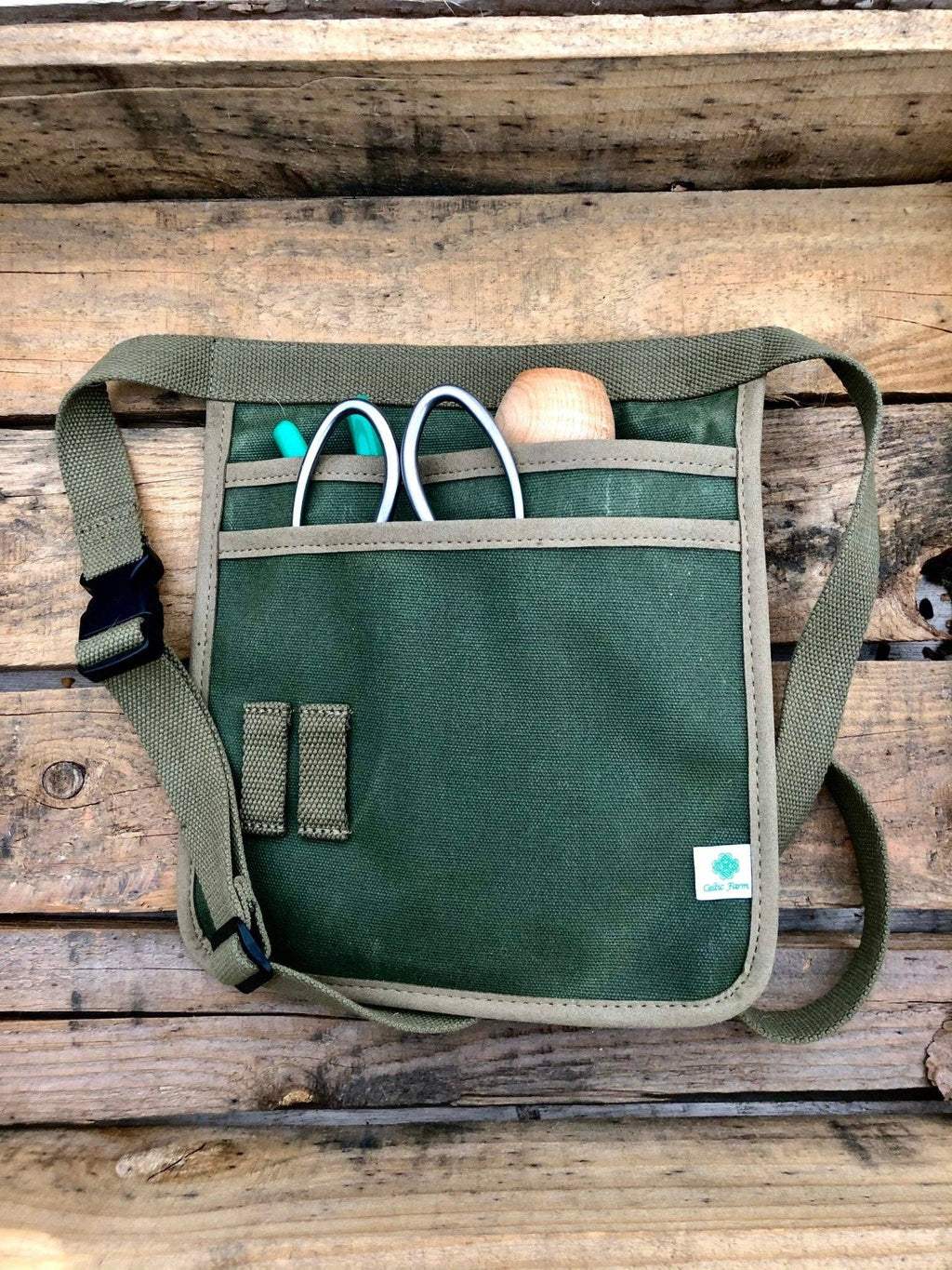 Front view of the olive-green garden tool belt with its adjustable strap and tools tucked into the pockets.