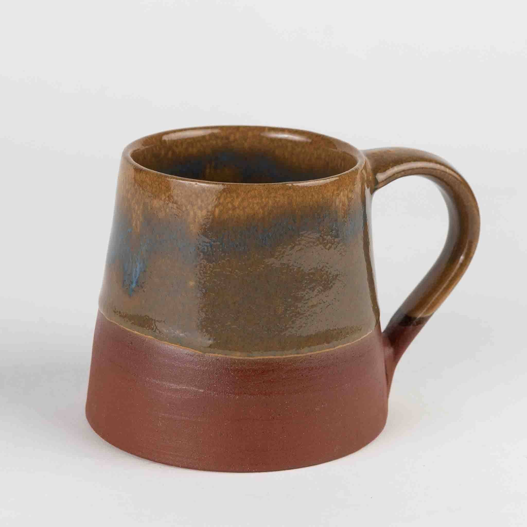 Angled side view with handle (gray bg): "Hand thrown terracotta ceramic mug with earthy brown glaze, blue drip accent, and unglazed terracotta base, handcrafted in Nepal by Ten Thousand Villages"
