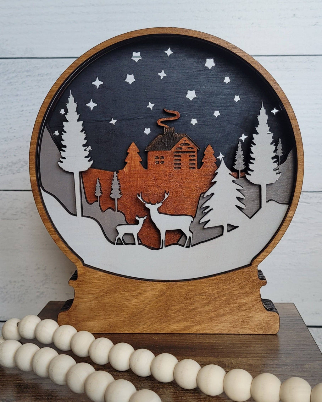 Deer wooden snowglobe on a wooden shelf with a white bead garland against a pale plank wall.