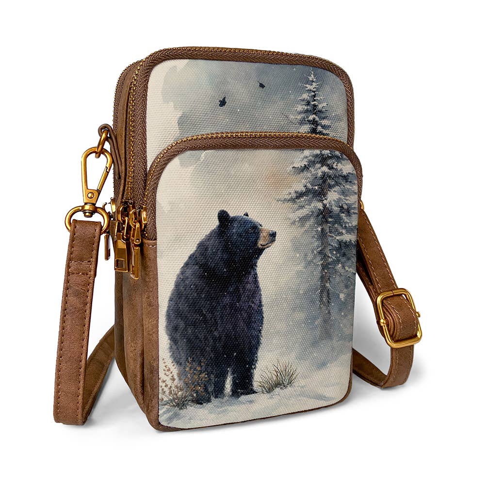 "Black bear in snow watercolor art canvas crossbody phone sling with snowy pine forest design, leather-look PU trim, antique brass zipper pulls and carabiner clip, and adjustable shoulder strap on white background"