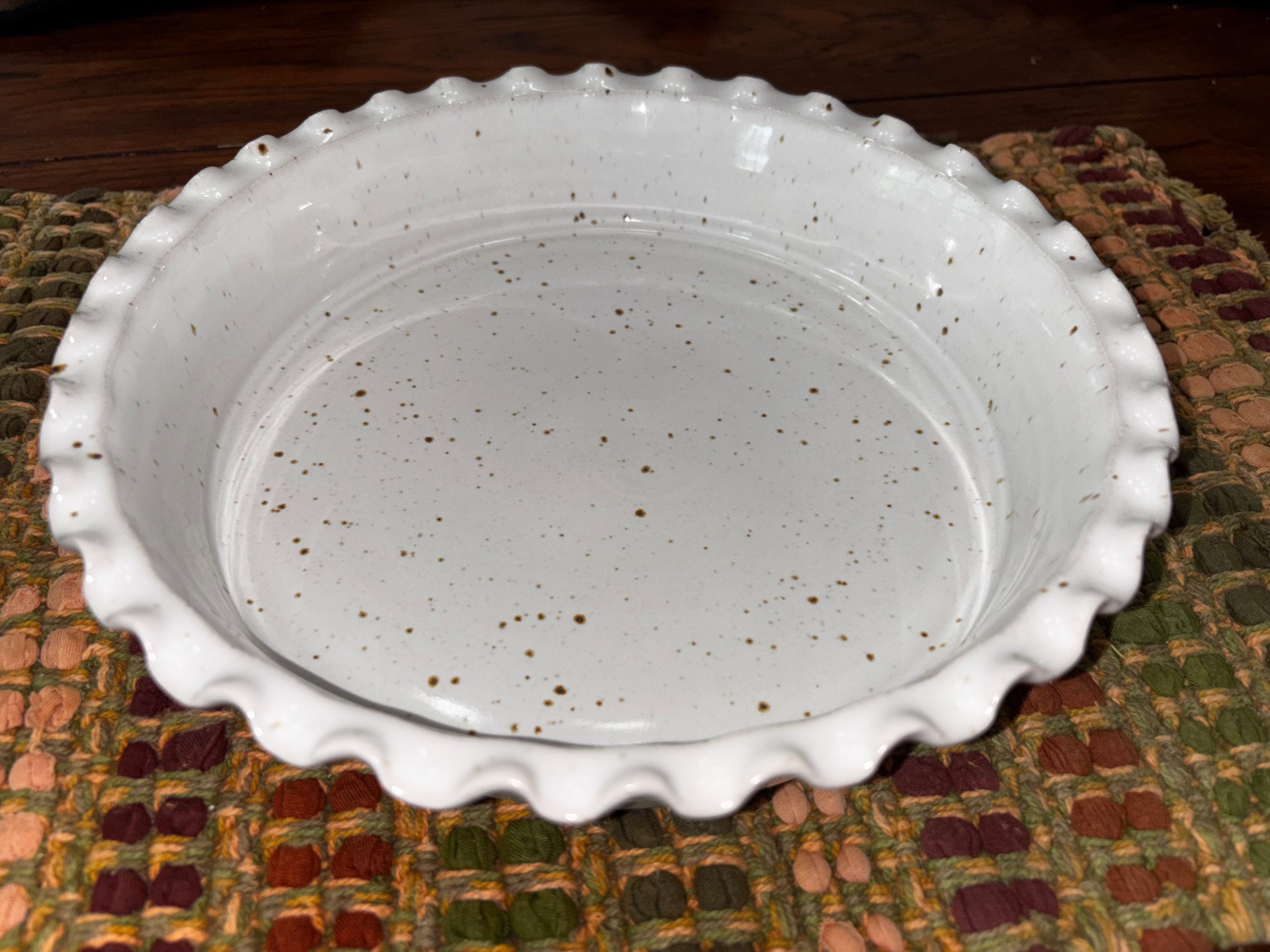 Angled view of a 9-inch hand-thrown white speckled stoneware deep dish pie plate with ruffled scalloped edge, showing depth