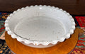 Top view of a 9-inch hand-thrown white speckled stoneware deep dish pie plate with ruffled scalloped edge on a wooden cutting board
