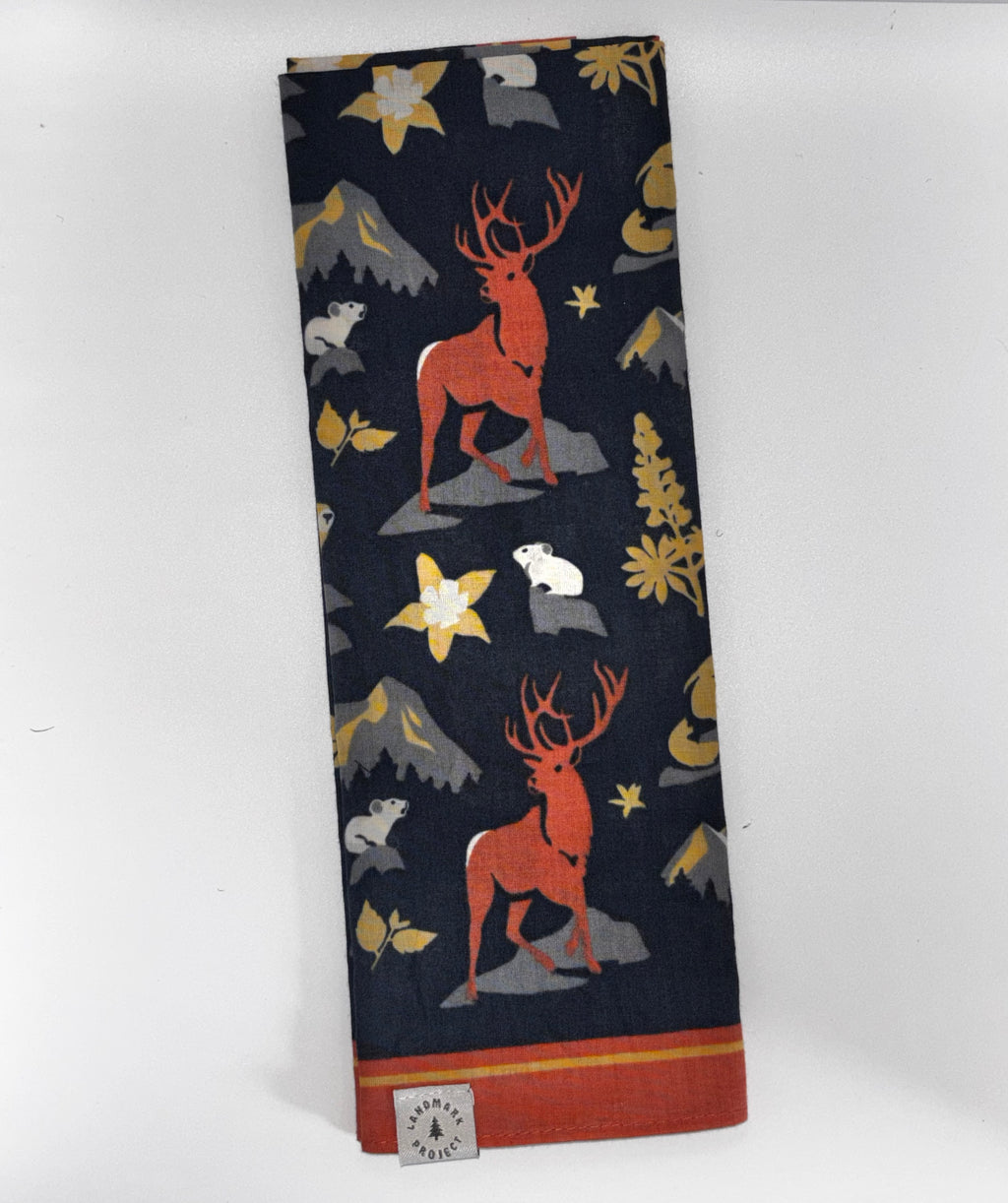 "Landmark Project Residents of the Rockies Bandana folded flat showing elk, mountains, stars, and wildlife print on navy with rust border and Landmark Project label"