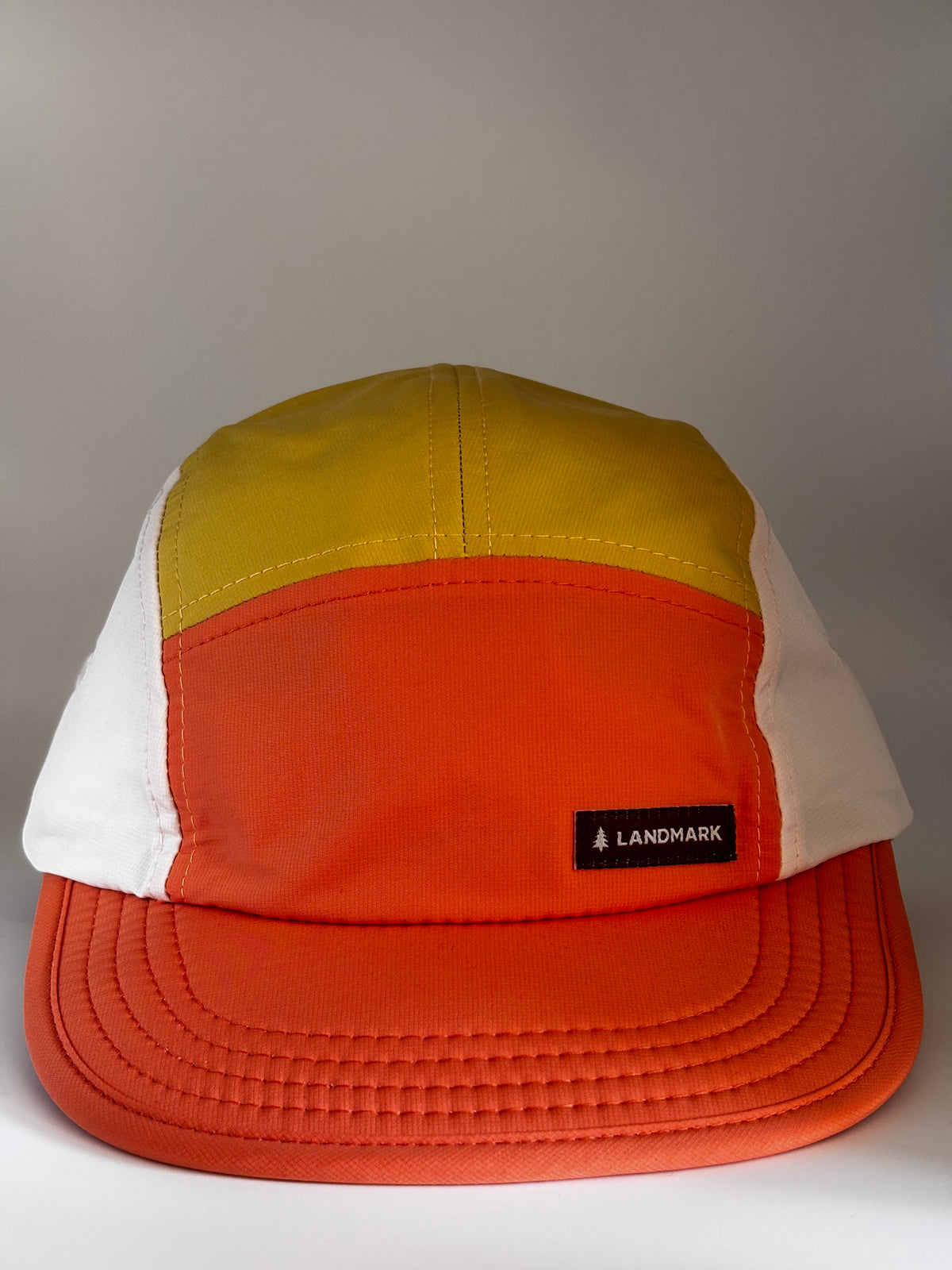 "Landmark Project Landmark Hike Hat front view in orange and yellow colorblock panels with white side panels, flat bill, and black Landmark label on front"