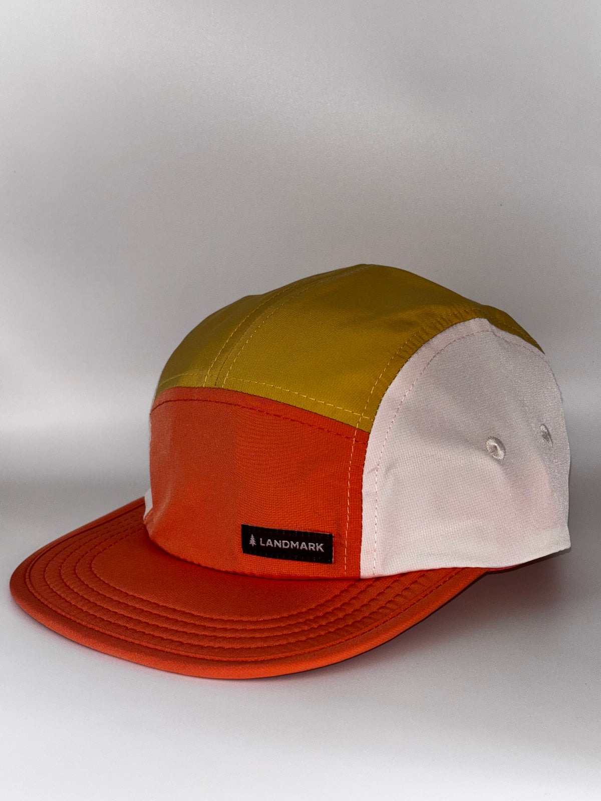  orange/yellow/white 5-panel, front with Landmark label): "Landmark Project Landmark Hike Hat in orange, yellow, and white colorblock 5-panel style, front view with Landmark label on brim"