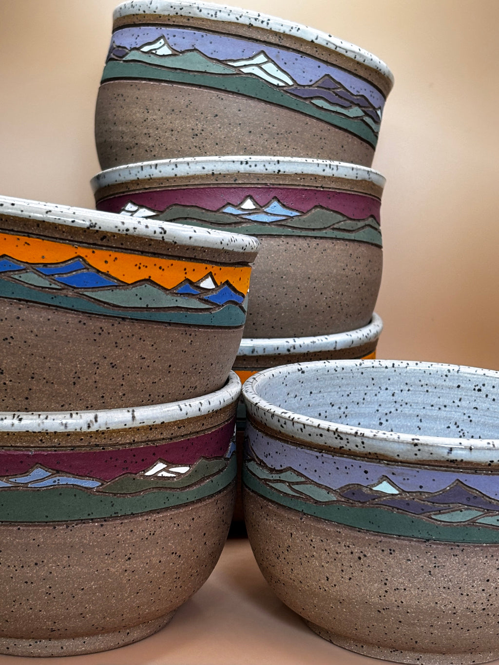 Close-up group — all colorways stacked in two columns:

"Close-up of all three Forest Jeannie mountain landscape stoneware bowl colorways — Crimson Ridge, Sunset Peak, and Twilight Summit — showing hand-painted detail and speckled texture"