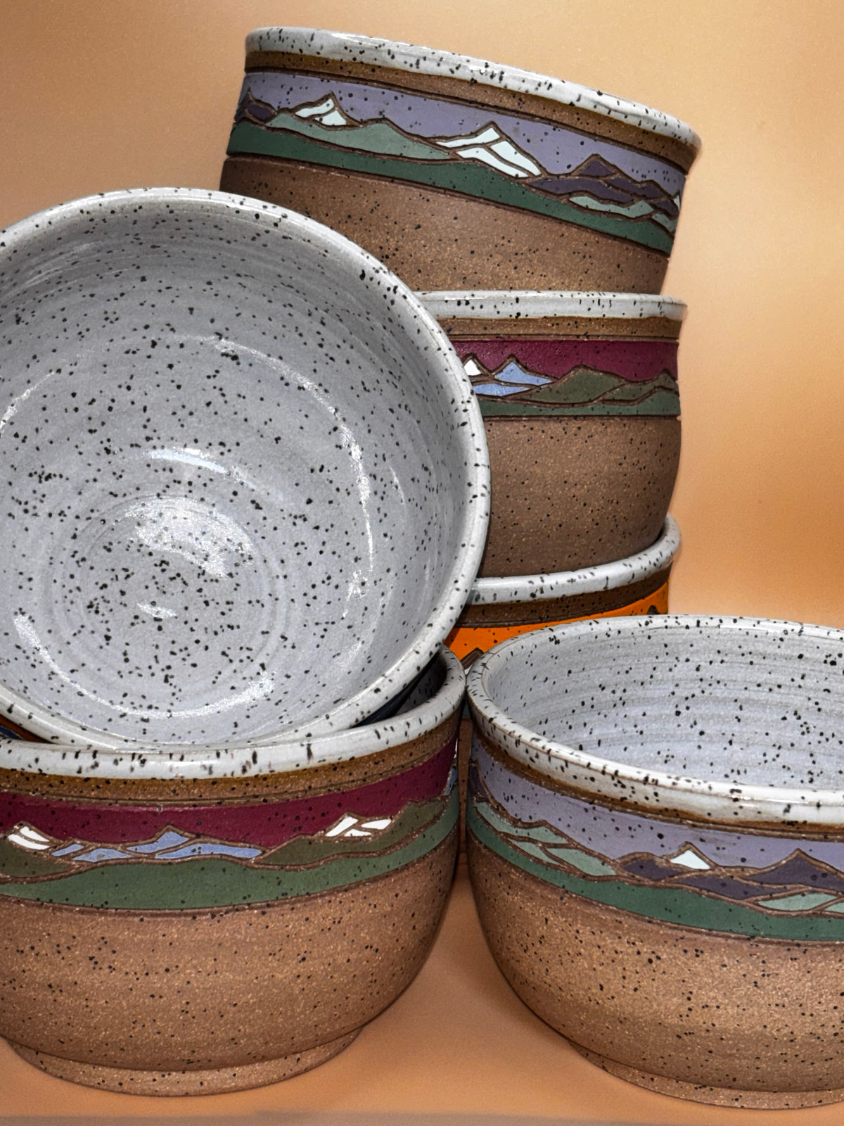 "All three colorways of Forest Jeannie handmade speckled stoneware mountain landscape bowls stacked together, showing speckled white interiors — handmade pottery by Forest Jeannie"