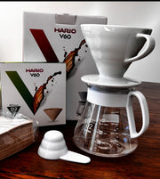 Hario V60 ceramic pour over coffee set with glass server, measuring spoon, and filter box displayed on a wooden surface
