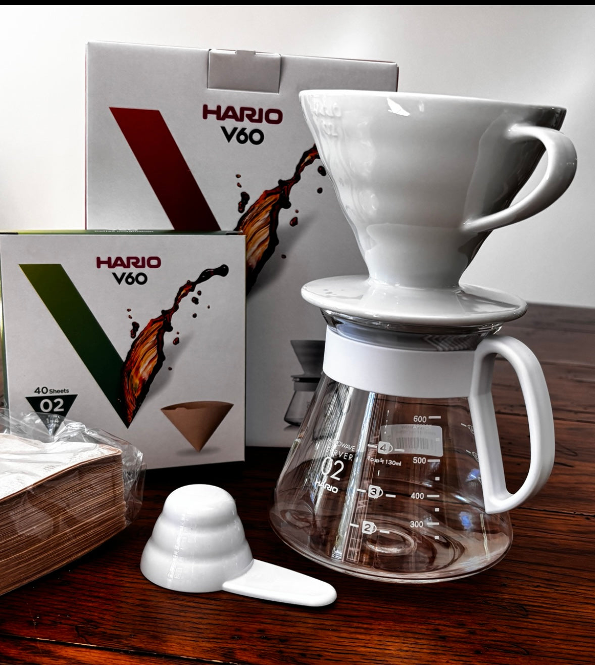 Hario V60 ceramic pour over coffee set with glass server, measuring spoon, and filter box displayed on a wooden surface