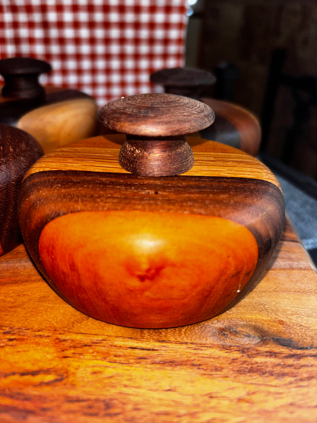 Handmade extra-large cathead biscuit cutter with a stunning deep amber and dark walnut striped wood body, smooth rounded form, and a dark textured knob on top, displayed on a rustic wood surface at an artisan market."