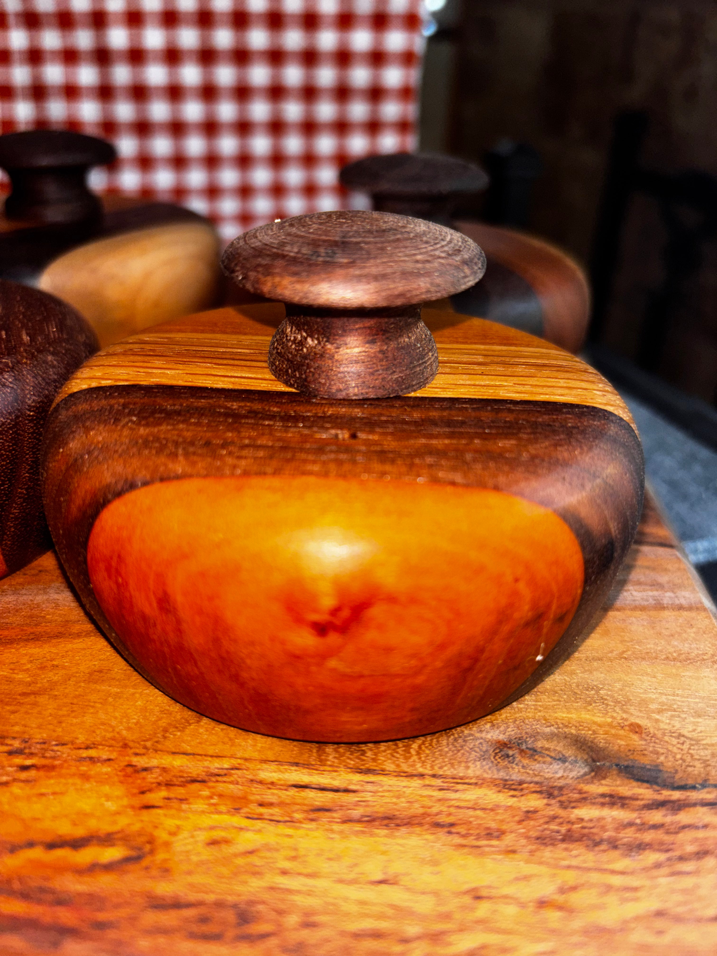 Handmade extra-large cathead biscuit cutter with a stunning deep amber and dark walnut striped wood body, smooth rounded form, and a dark textured knob on top, displayed on a rustic wood surface at an artisan market."
