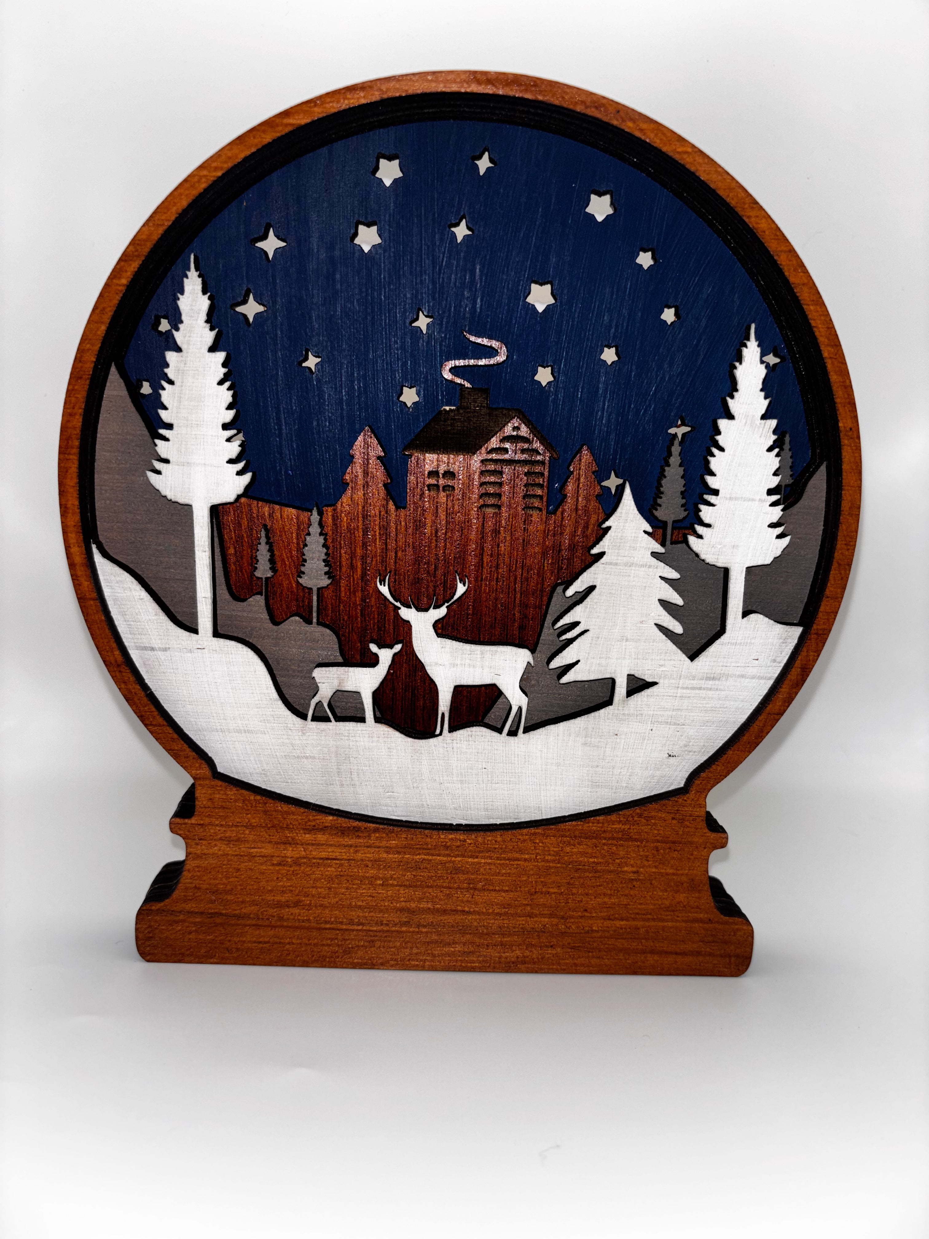  Winter Deer wooden snow globe with two deer, snowy pine trees, a cabin, and stars against a navy sky.