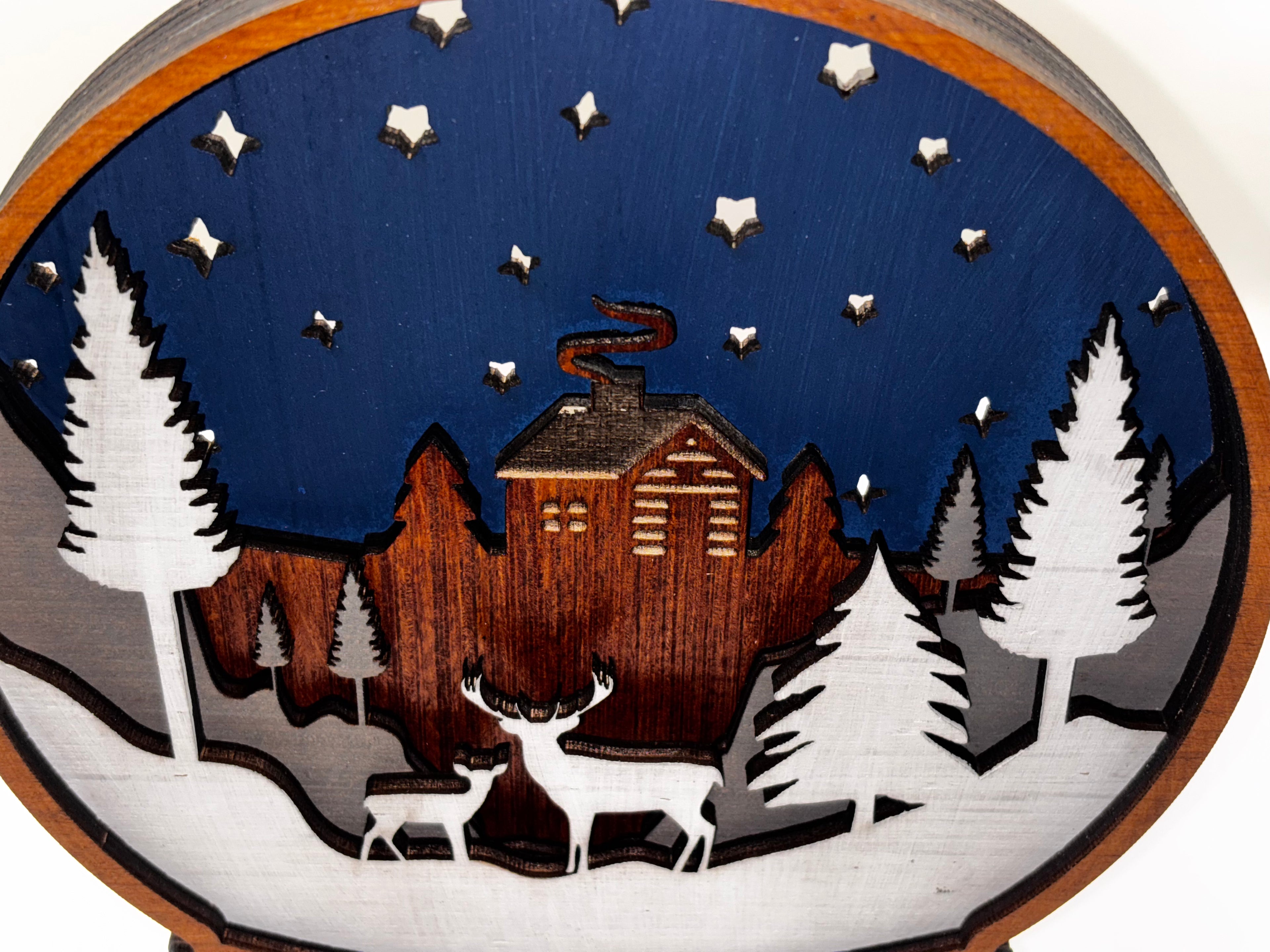 Close-up of the wooden snowglobe’s starry navy sky, rustic cabin, white pine trees, and two deer.