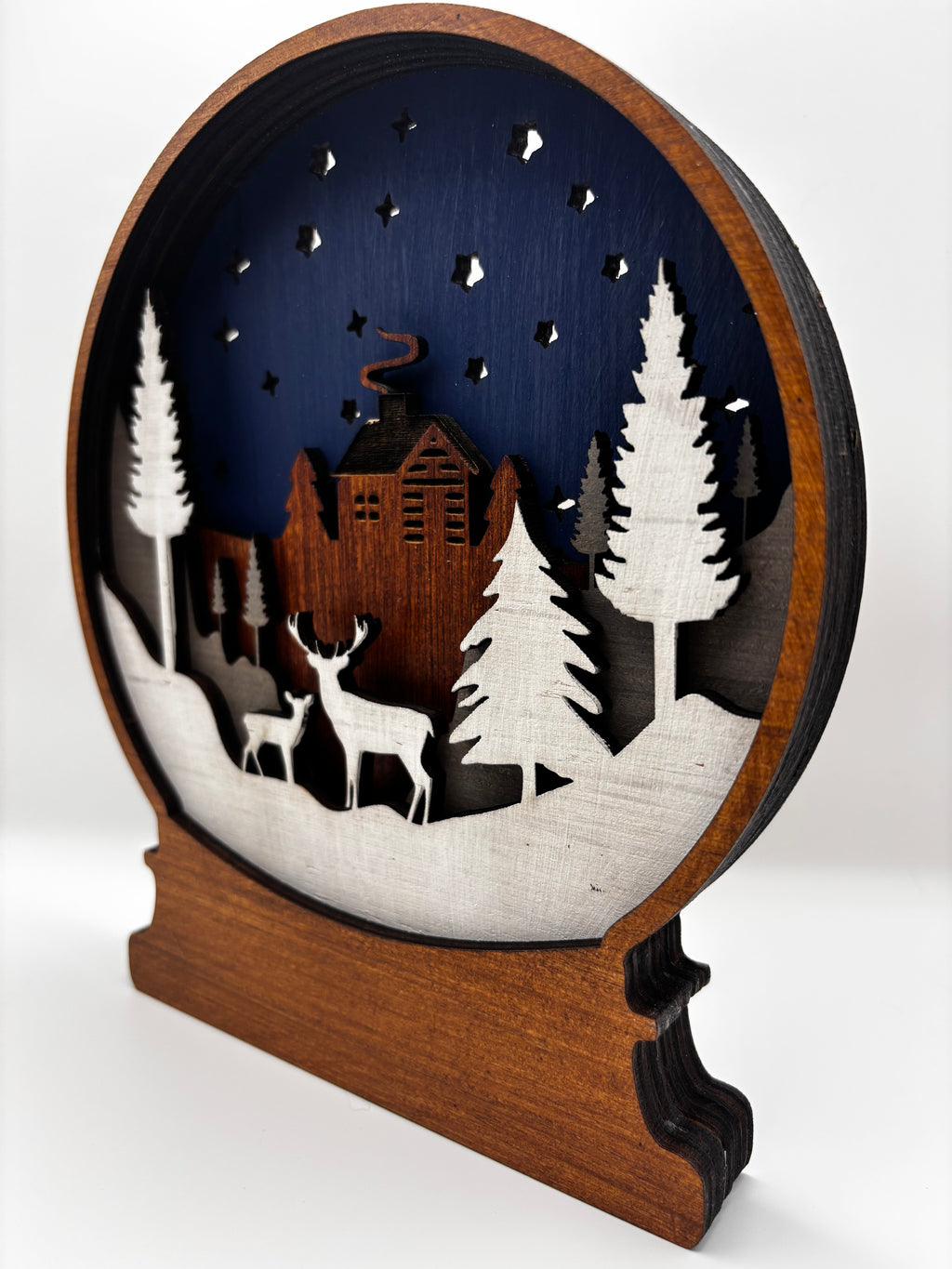 Angled view of Winter Deer wooden snow globe showing layered depth, snowy trees, two deer, and a cabin.