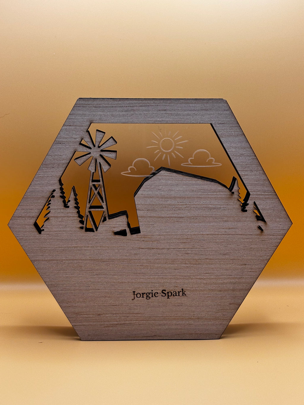 Back of the hexagonal farm artwork showing wood grain, the Jorgie Spark mark, and clear acrylic with an etched sun and clouds.