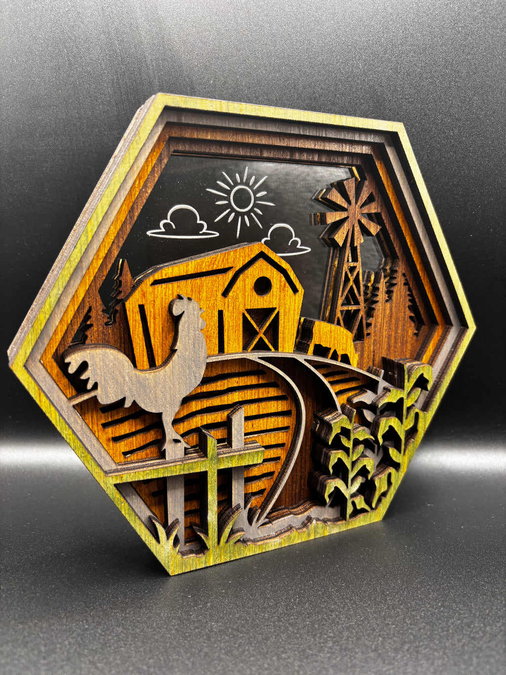 Angled view of the Farm Scene Hexagon showing layered wood depth, a rooster on a fence, yellow barn, and windmill.