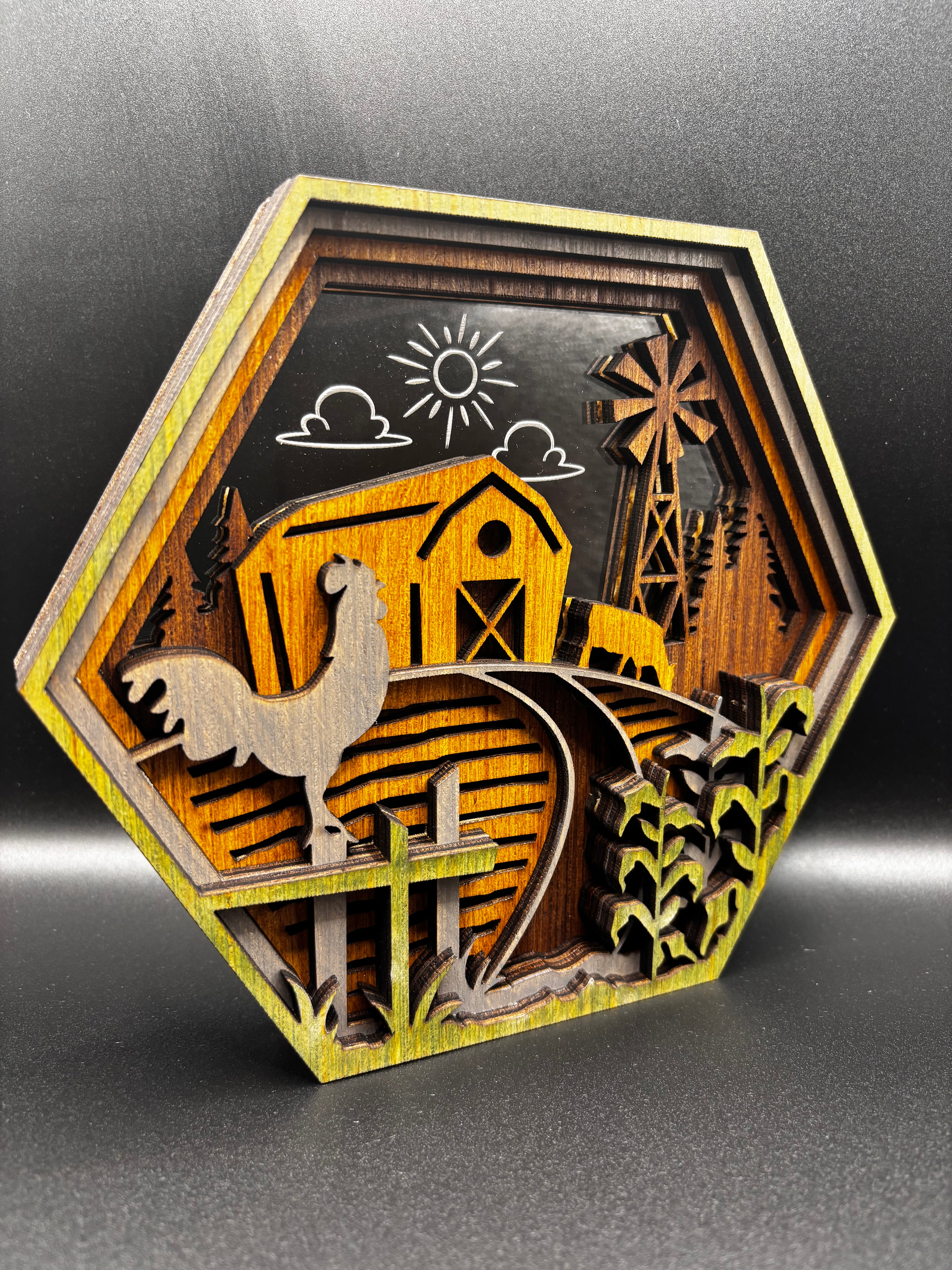 Angled view of the Farm Scene Hexagon showing layered wood depth, a rooster on a fence, yellow barn, and windmill.