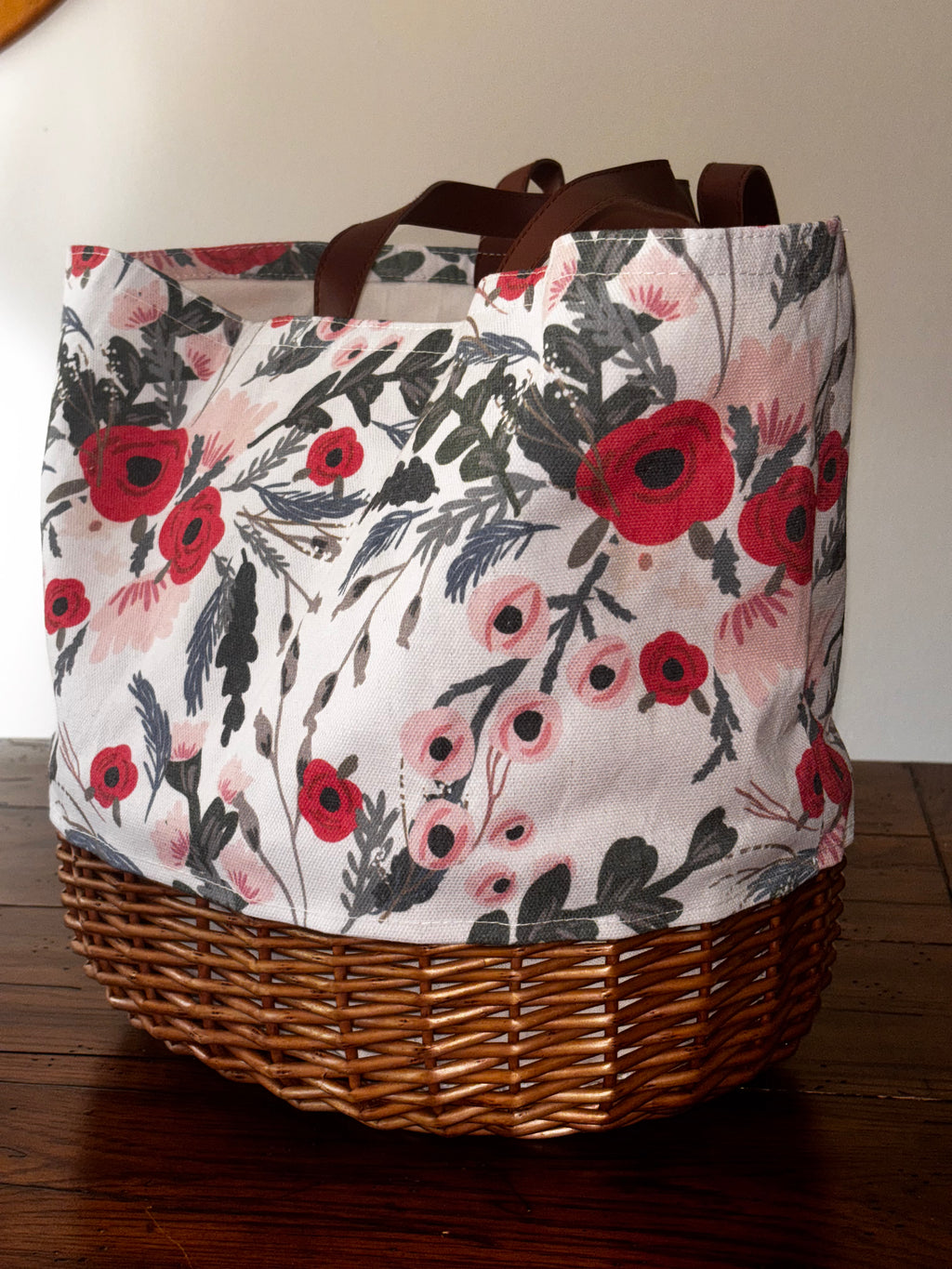 Floral Promenade picnic tote with brown handles and a woven willow base on a wooden table.