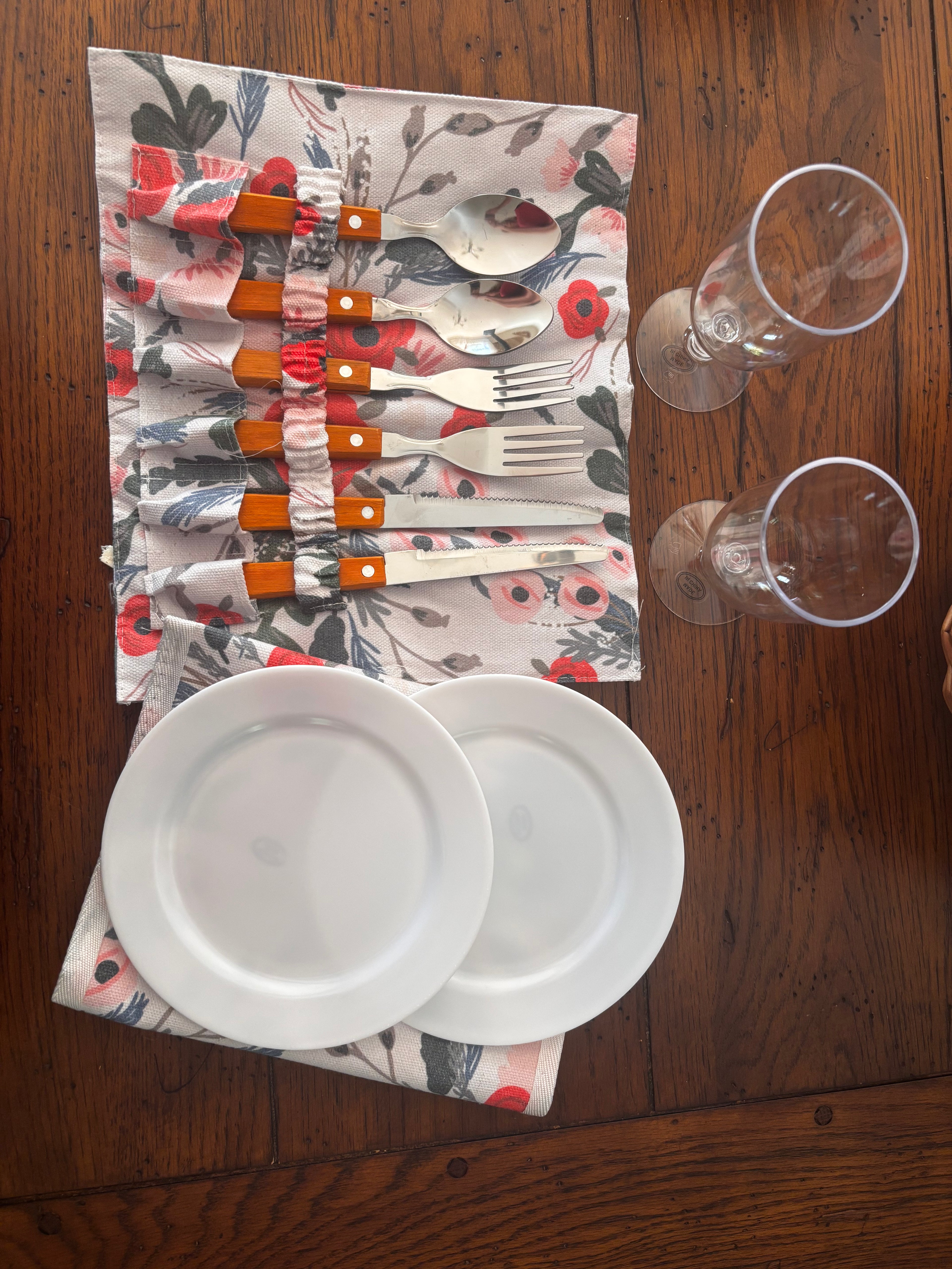 Overhead view of two white plates, two clear drinking glasses, and wood-handled cutlery in a floral holder.