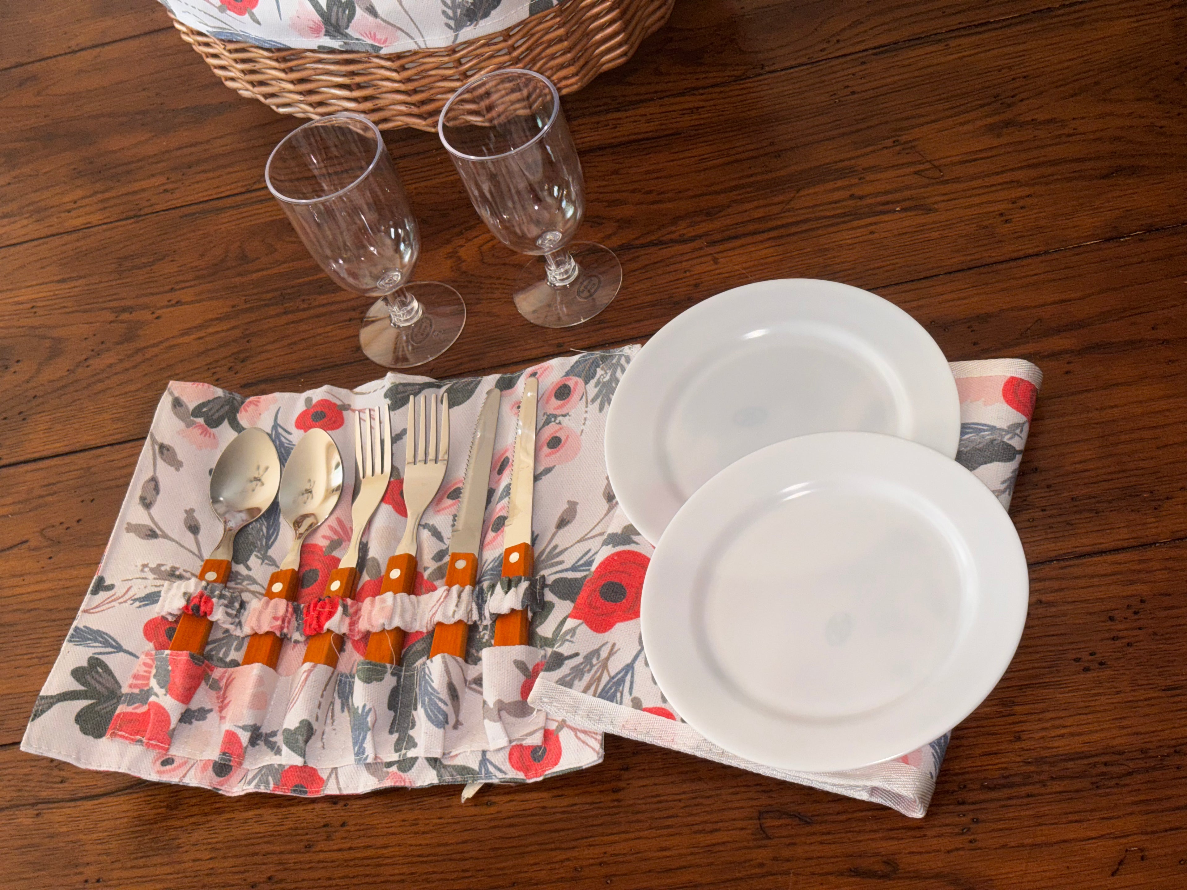 Picnic tableware for two with white plates, two clear drinking glasses, and six utensils in a matching floral holder.