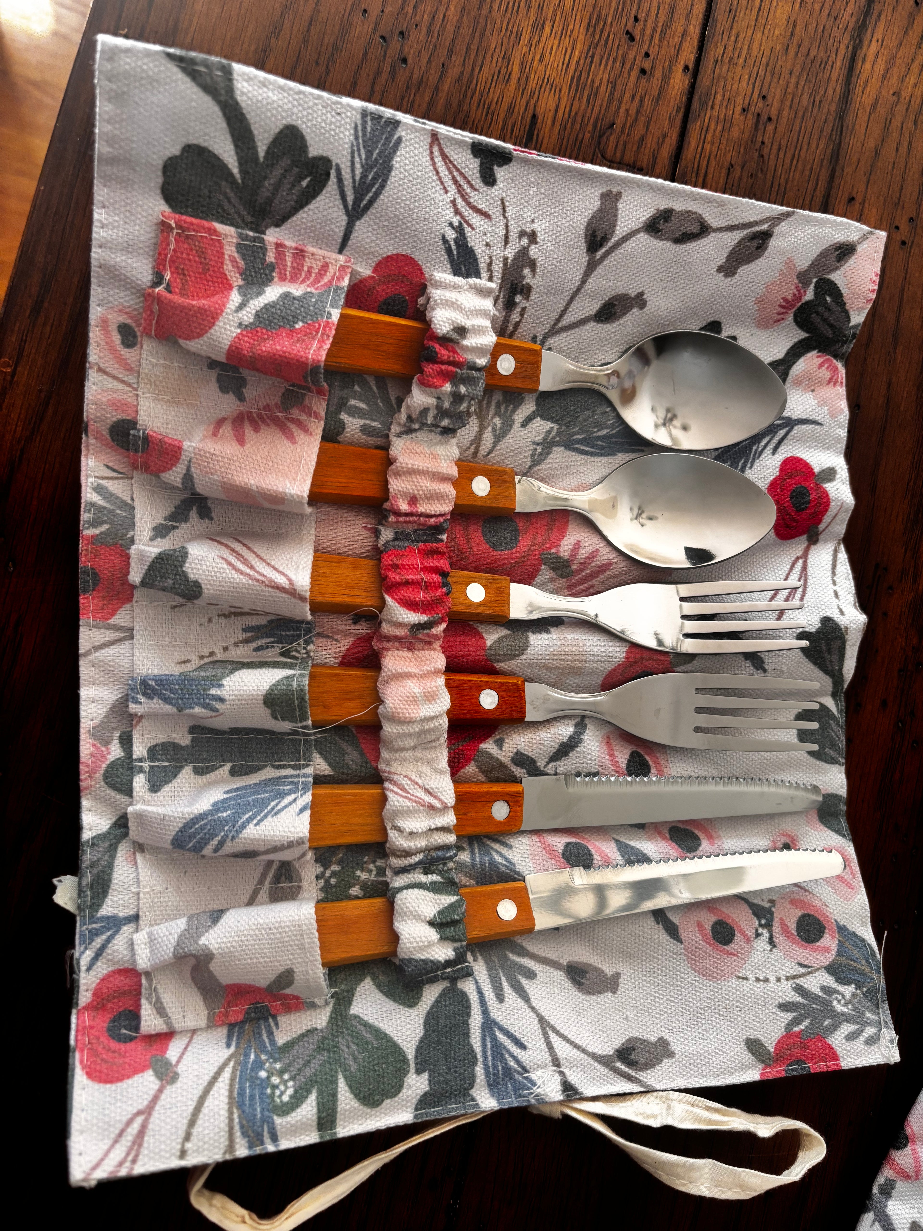Open floral cutlery holder containing two spoons, two forks, and two knives with wood-toned handles.