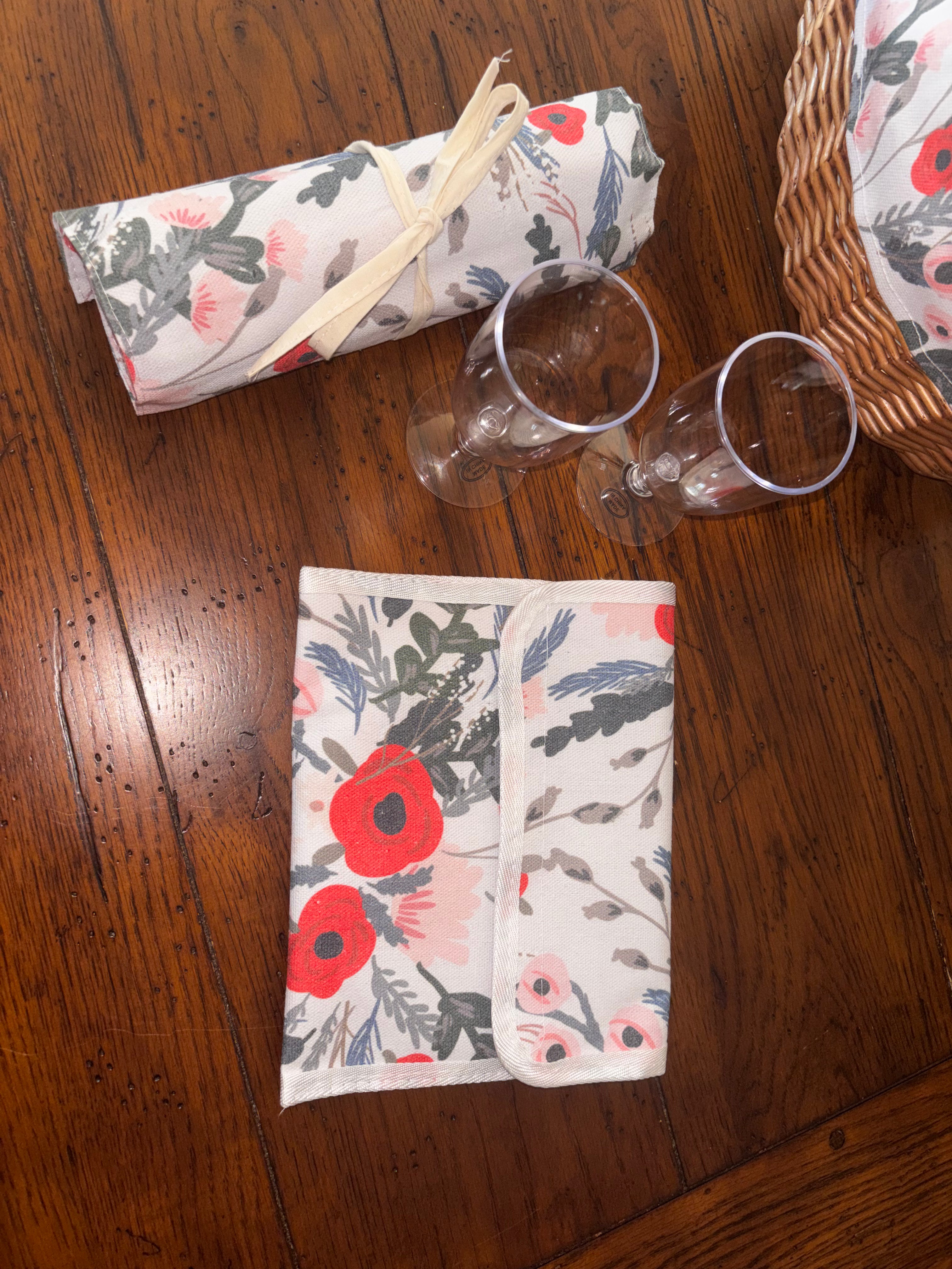 Packed floral plate sleeve and rolled cutlery holder beside two clear drinking glasses and the tote’s woven base.
