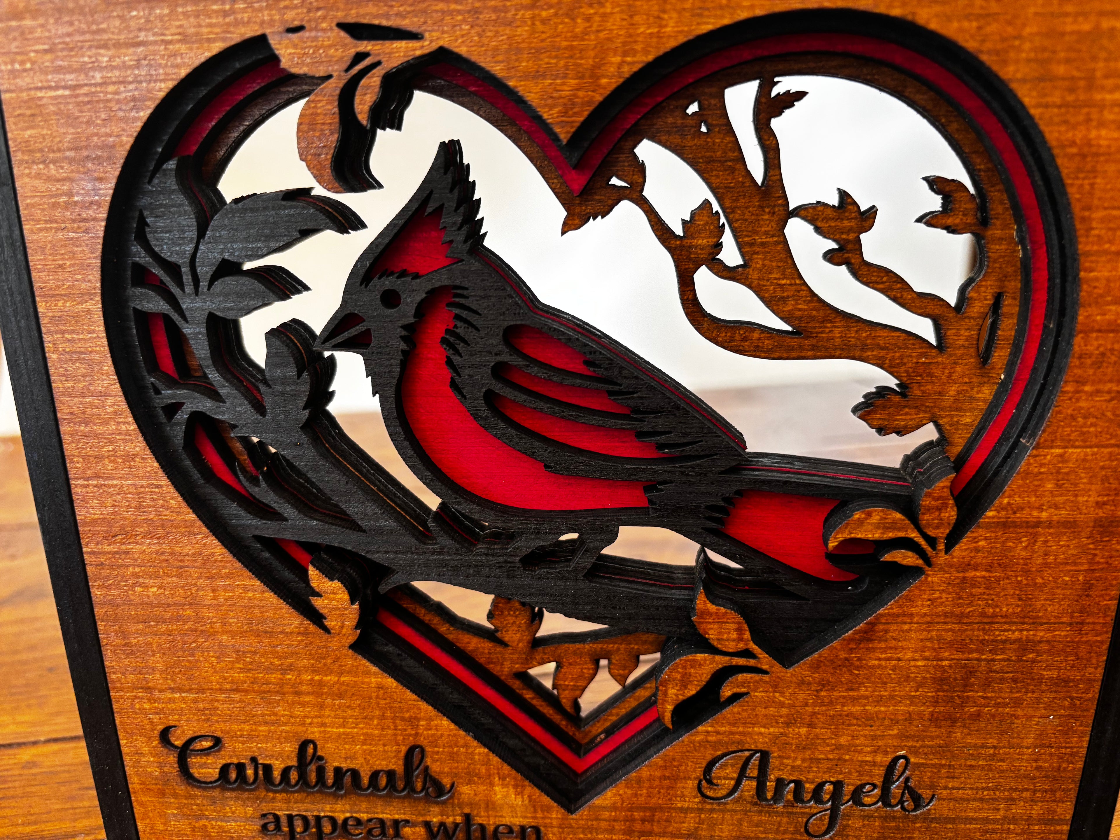 Close-up of a red cardinal and leafy branches within the heart-shaped opening of the layered wood plaque.