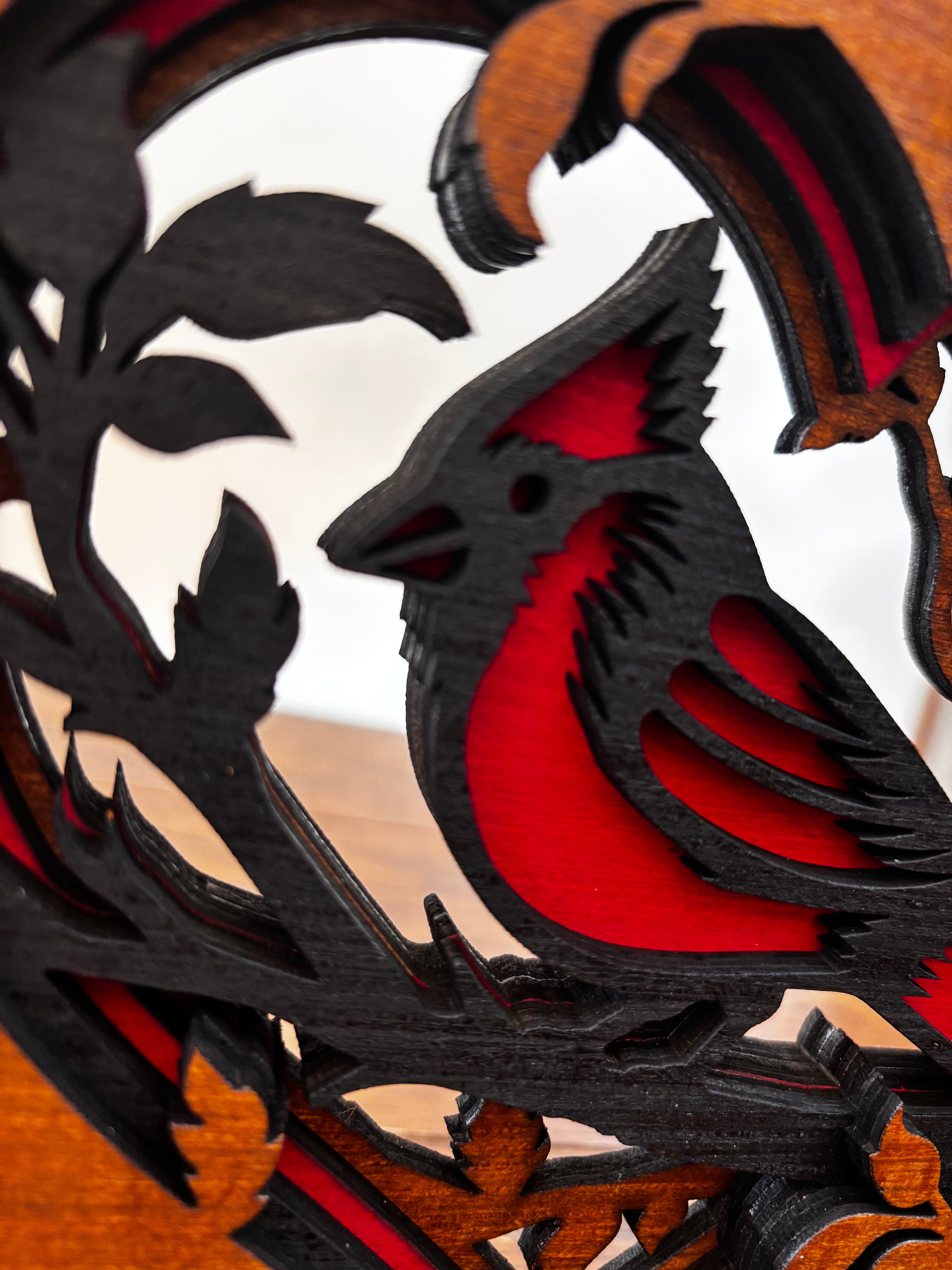 Detail of the cardinal’s head and red breast beneath black wood layers, beside carved leaves.