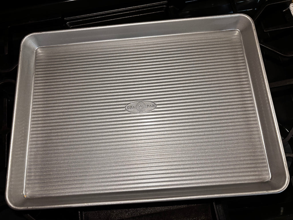Angled view of the USA Pan half sheet pan with embossed center logo and continuous raised rim.