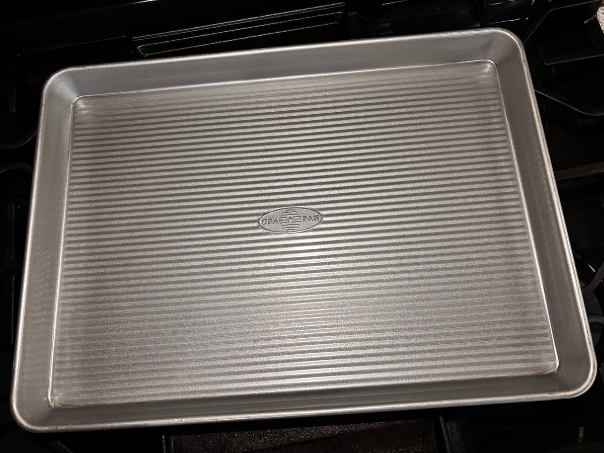 Angled view of the USA Pan half sheet pan with embossed center logo and continuous raised rim.