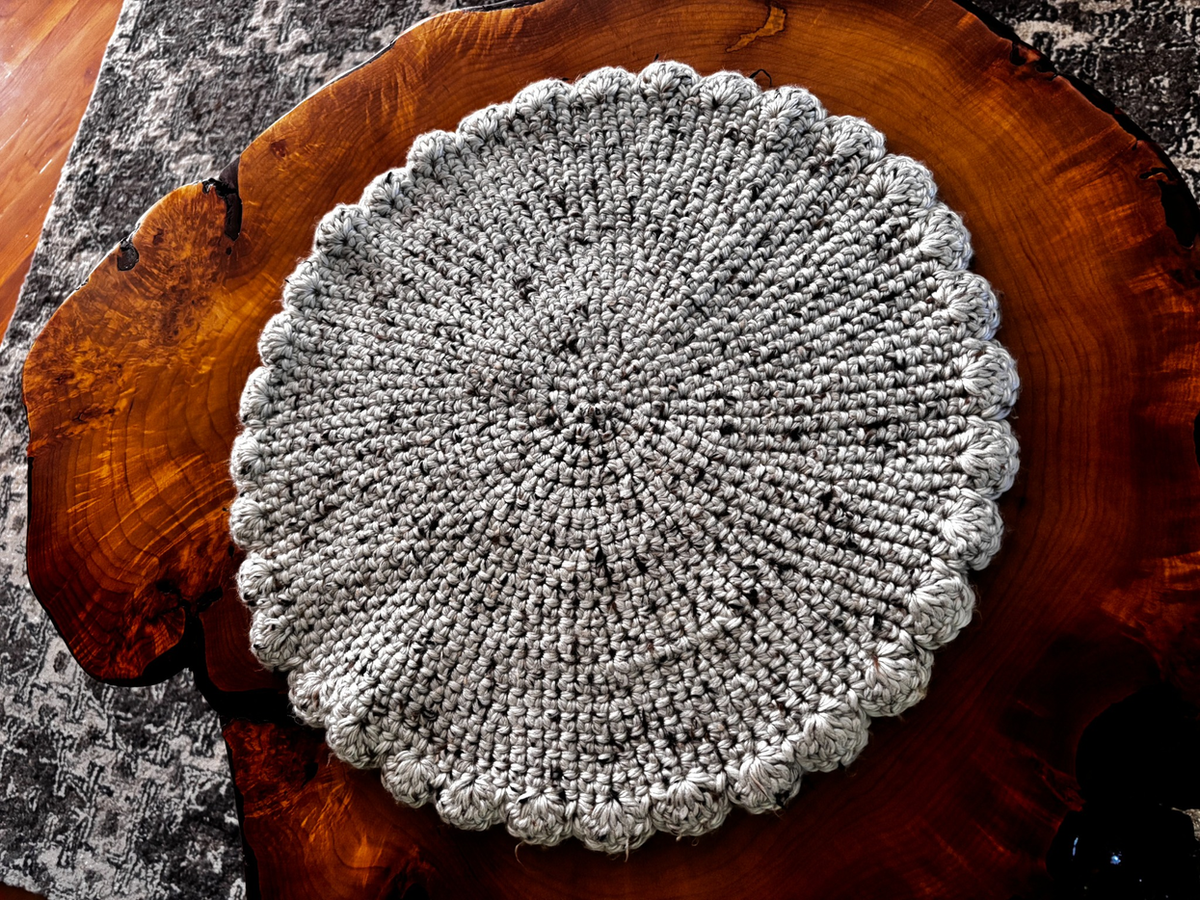 Overhead view of the natural tweed wool blend crochet cat lounger with scalloped edge, displayed on a live-edge wood slab, handmade by Sleeping Whiskers Studio.