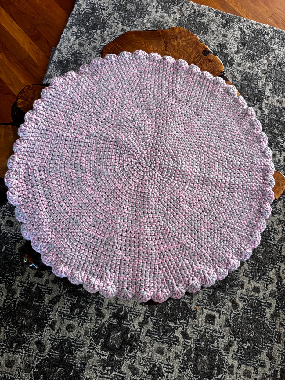 Overhead view of a large round pink and gray hand-crocheted cat lounger with a decorative scalloped edge, handmade by Sleeping Whiskers Studio.