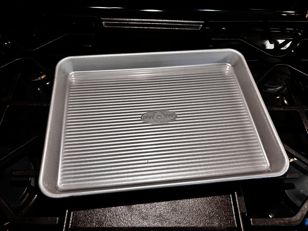 USA Pan quarter sheet pan on a dark stovetop, showing its compact rectangular shape and corrugated base.