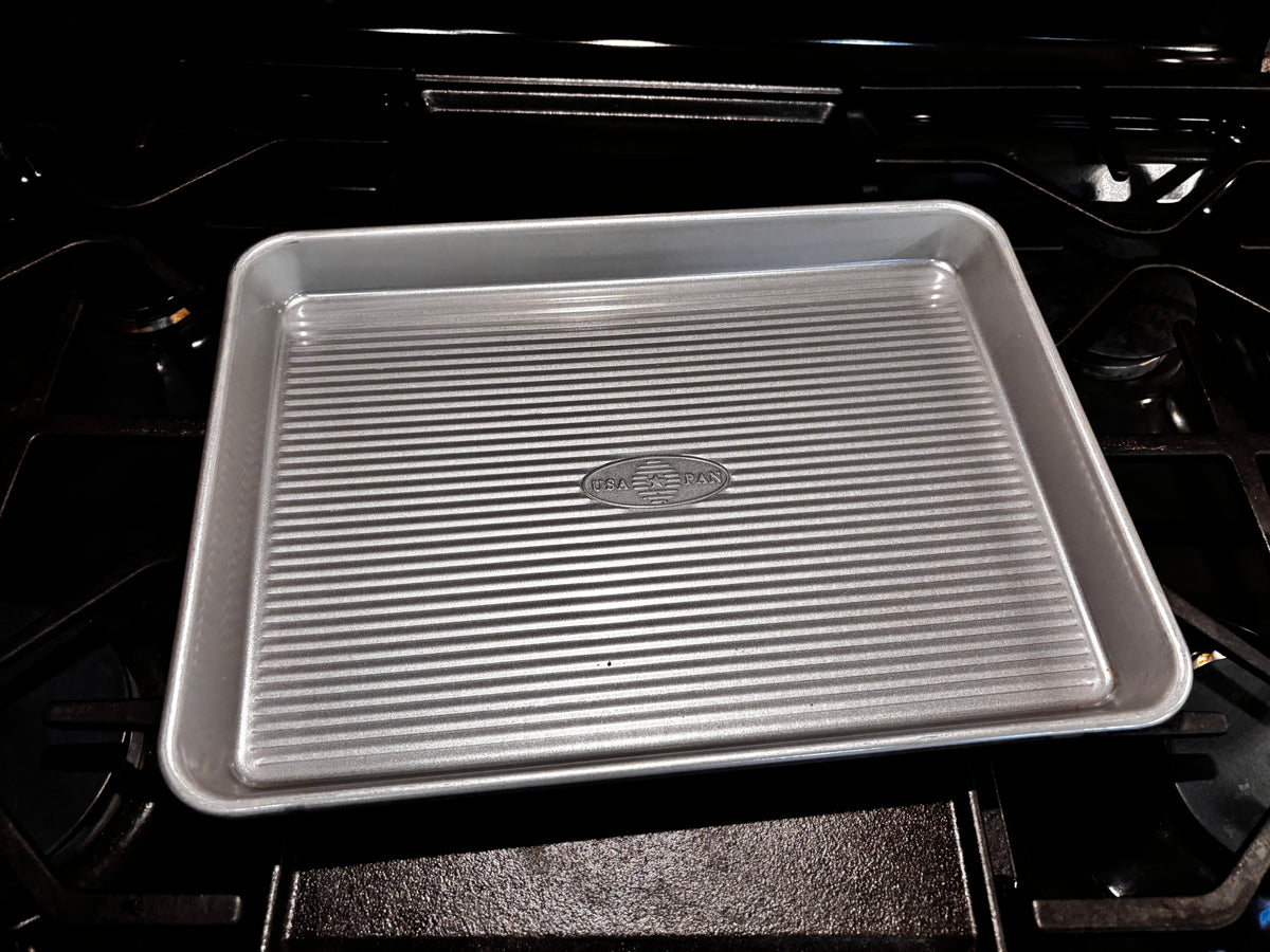 USA Pan quarter sheet pan on a dark stovetop, showing its compact rectangular shape and corrugated base.