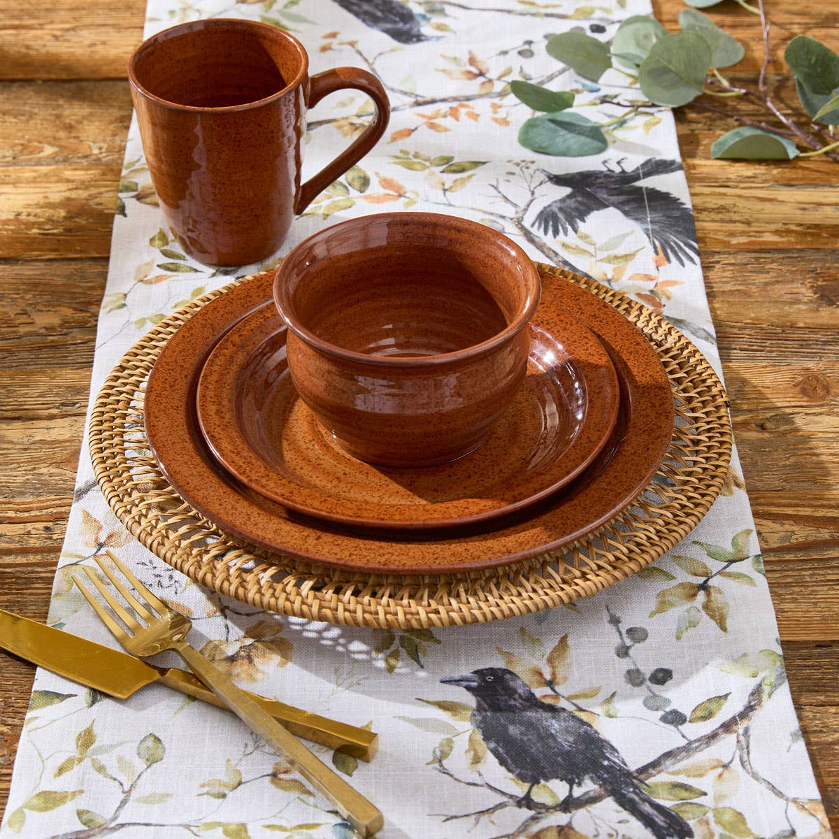 Park Designs Sinclair Tomato Soup salad plate and cereal bowl on a rattan charger with a botanical bird table runner, matching mug, and gold cutlery on a farmhouse wood table"