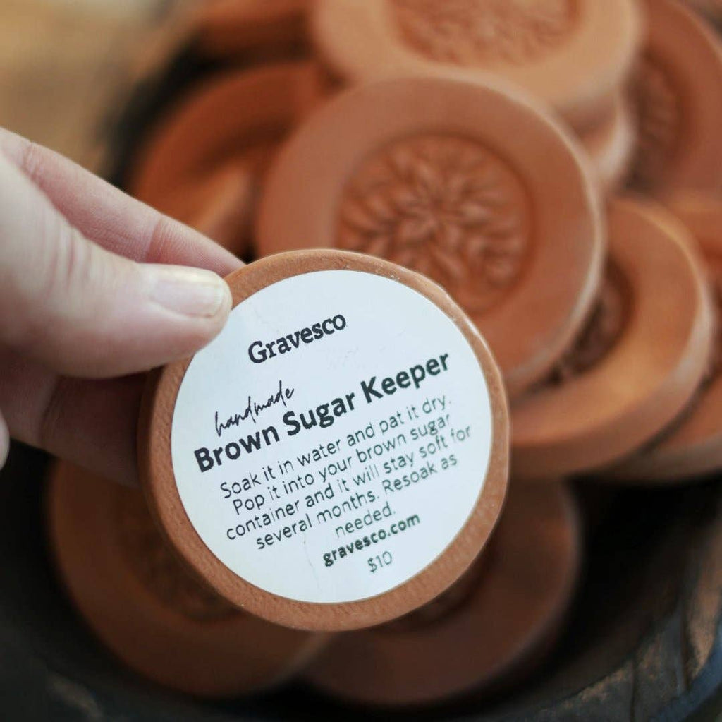 Hand holding a single Gravesco handmade terracotta brown sugar keeper showing detailed floral medallion carving, with more in background"